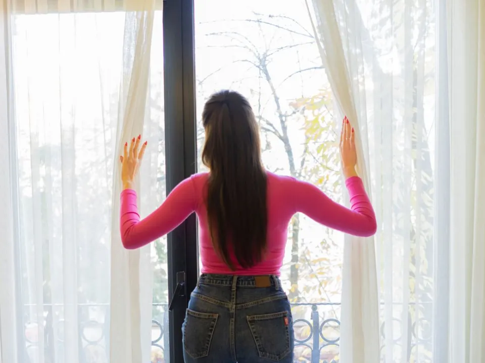 A woman opening the curtains to let in the morning light