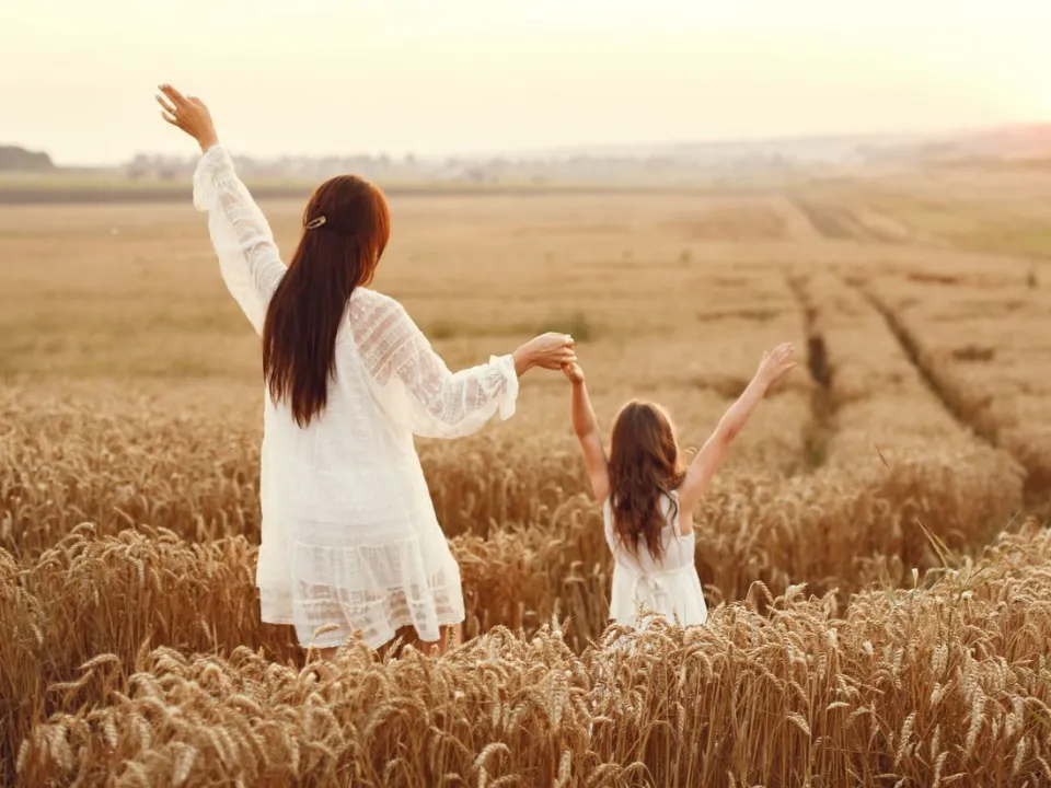 A mother and daughter walking hand in hand through a wheat field